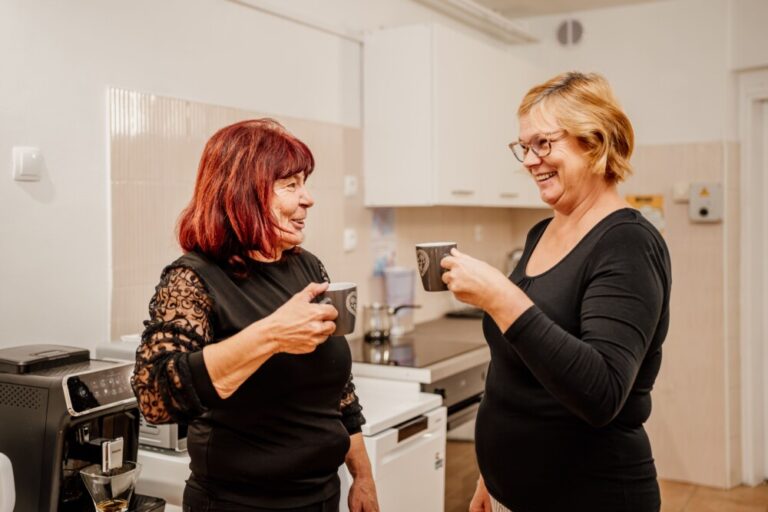 Dve osebi pijeta kavo in sta nasmejani.