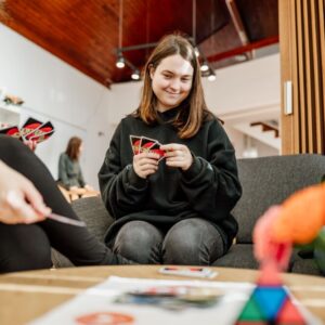 Tri osebe sedijo okrog manjše mize in igrajo igro s kartami.