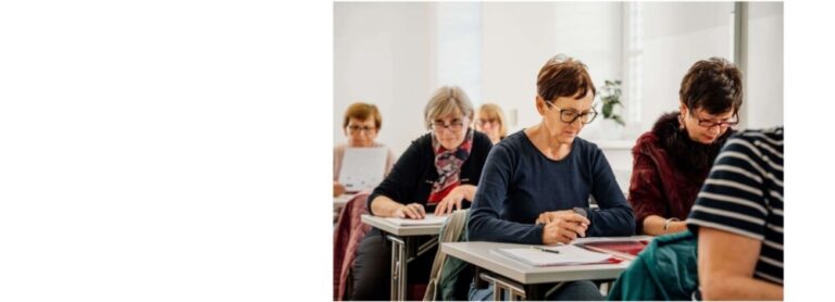 Osebe sedijo v predavalnici in poslušajo predavatelja.