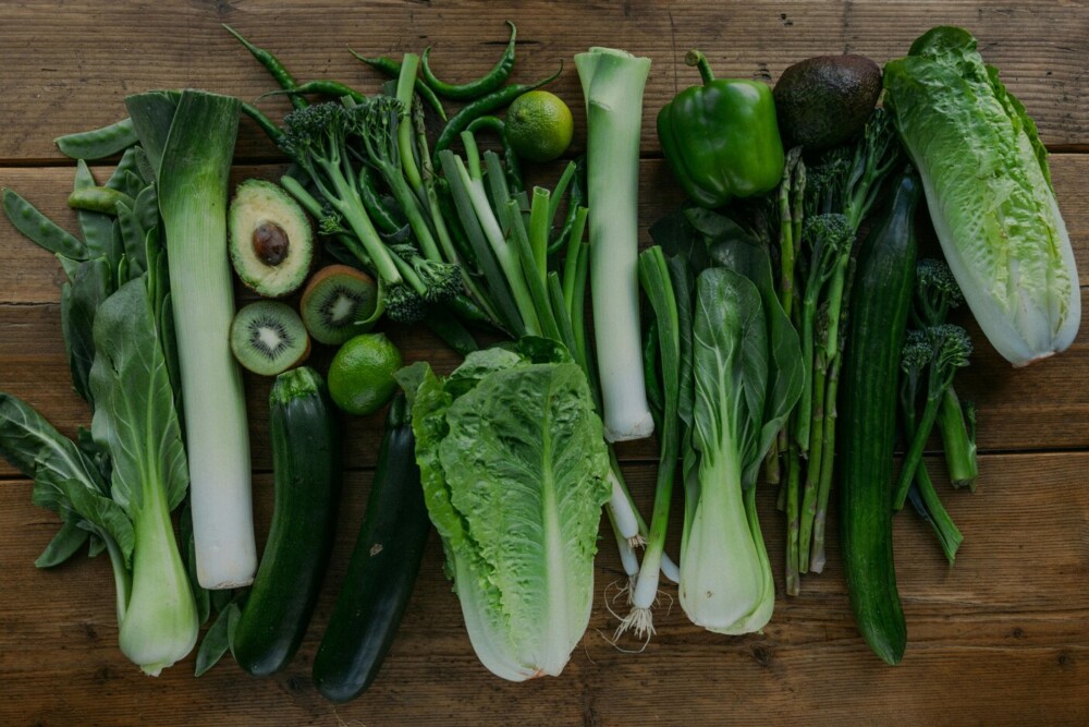 Na leseni mizi je razporejena zelena zelenjava in sadje (por, bučke solata, grah, avokado, kivi, limeta, brokoli, mlada čebula, paprika, šparglji in kumara).