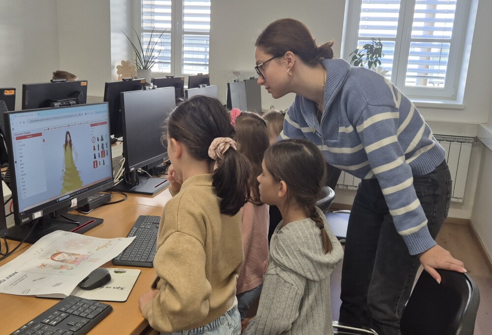 V računalniški učilnici so otroci in učiteljica, ki na računalniku ustvarjajo digi junake.