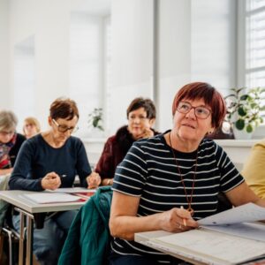 Osebe sedijo v predavalnici in poslušajo predavatelja