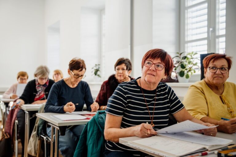Osebe sedijo v predavalnici in poslušajo predavatelja
